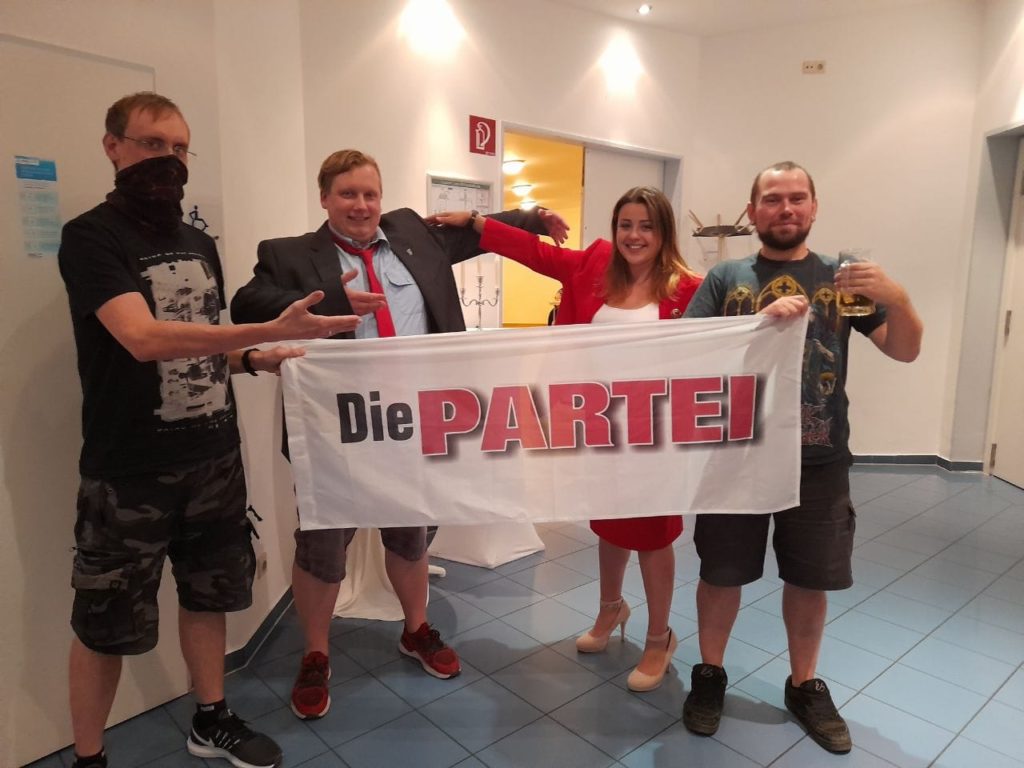 Vier Menschen, die mit einer PARTEI-Fahne posieren